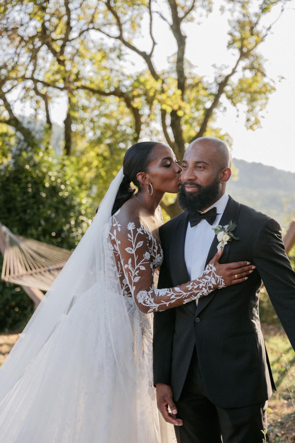 A bride kisses her groom on the cheek in front of a hammock.