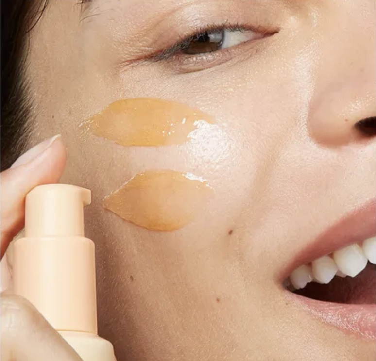 Lady squirting orange serum on cheeks