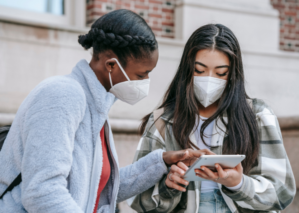 Two college students looking at a tablet outside a brick academic building.