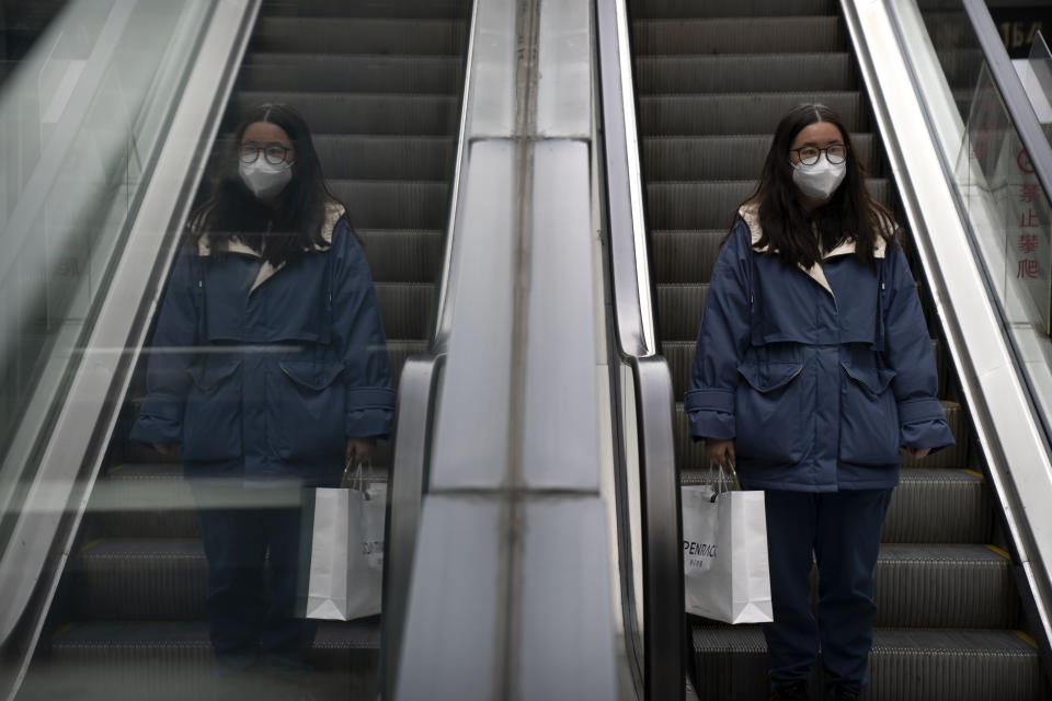 A woman wearing a face mask rides an escalator at a shopping and office complex in Beijing, Wednesday, Jan. 11, 2023. Japan and South Korea on Wednesday defended their border restrictions on travelers from China, with Tokyo criticizing China's move to suspend issuing new visas in both countries as a step unrelated to virus measures. (AP Photo/Mark Schiefelbein)