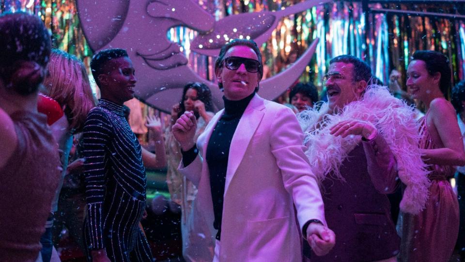 Ewan McGregor in a white suit dancing among people bathed in purple light in a still from Netflix's Halston.