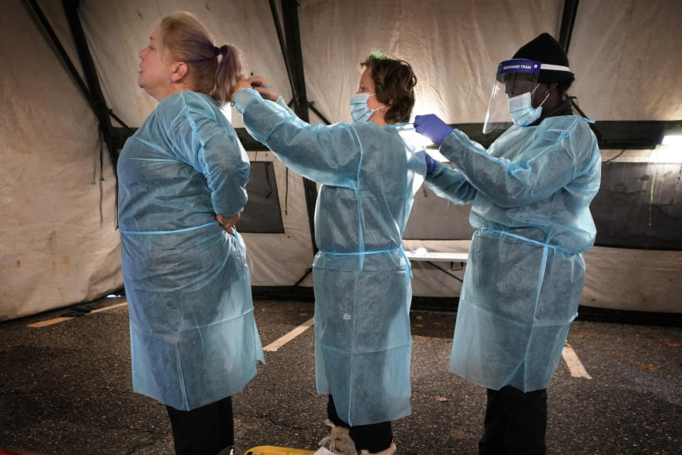 Testers help each other with their personal protective equipment at the start of their shift at a mobile testing location for COVID-19, Tuesday, Dec. 8, 2020, in Auburn, Maine. More than 14,000 Mainers have been diagnosed with the disease and 239 have died. (AP Photo/Robert F. Bukaty)