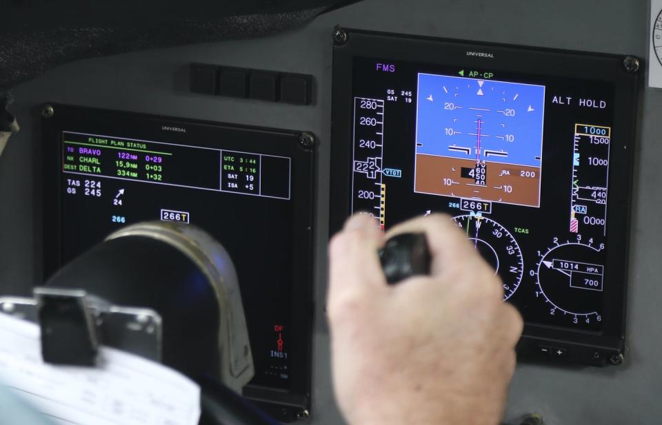 A hand on an aircraft yoke in front of a multicolor display panel