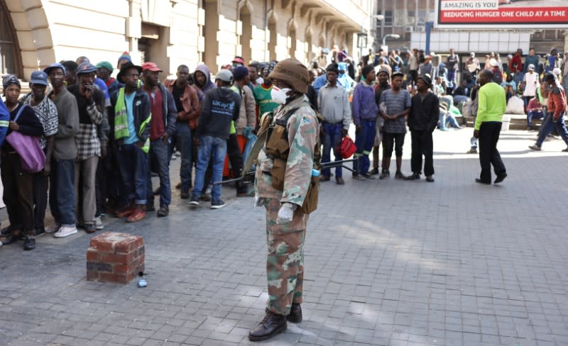 A member of the South African National Defense Forces keeps watch as homeless men stand in a queue in Johannesburg