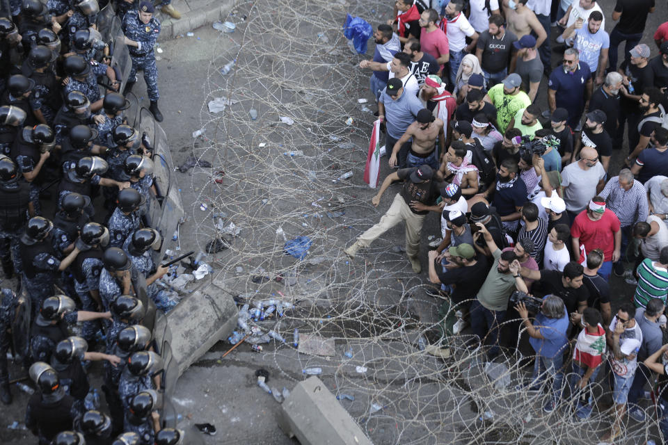 Riot police stand guard as anti-government protesters try to remove a barbed-wire barrier to advance towards the government buildings during a protest in Beirut, Lebanon, Saturday, Oct. 19, 2019. The blaze of protests was unleashed a day earlier when the government announced a slate of new proposed taxes, including a $6 monthly fee for using Whatsapp voice calls. The measures set a spark to long-smoldering anger against top leaders from the president and prime minister to the numerous factional figures many blame for decades of corruption and mismanagement. (AP Photo/Hassan Ammar)