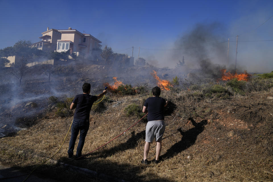 Residents spray water with a hose as fire burns near houses in the area of Drafi east of Athens on Wednesday, July 20, 2022. Hundreds of people were evacuated from their homes late Tuesday as a wildfire threatened mountainside suburbs northeast of Athens. Firefighters battled through the night, struggling to contain the blaze which was being intensified by strong gusts of wind. (AP Photo/Thanassis Stavrakis)