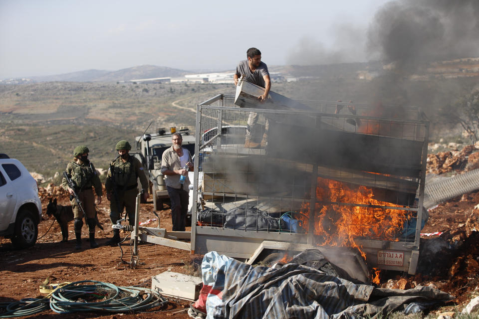 Israeli settler tries to extinguish a trailers set on fire by Palestinians during a protest against the expansion of Jewish settlements near the West Bank town of Salfit, Monday, Nov. 30, 2020. In years to come, Israelis will be able to commute into Jerusalem and Tel Aviv from settlements deep inside the West Bank via highways, tunnels and overpasses that cut a wide berth around Palestinian towns. Rights groups say the new roads that are being built will set the stage for explosive settlement growth, even if President-elect Joe Biden's administration somehow convinces Israel to curb its housing construction. (AP Photo/Majdi Mohammed)