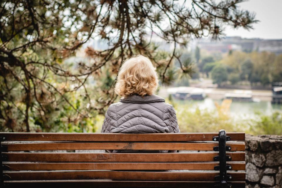 An older woman sitting on a bench, facing away from the camera