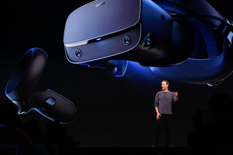 Facebook CEO Mark Zuckerberg stands on stage in front of a screen displaying the Oculus Quest headset.