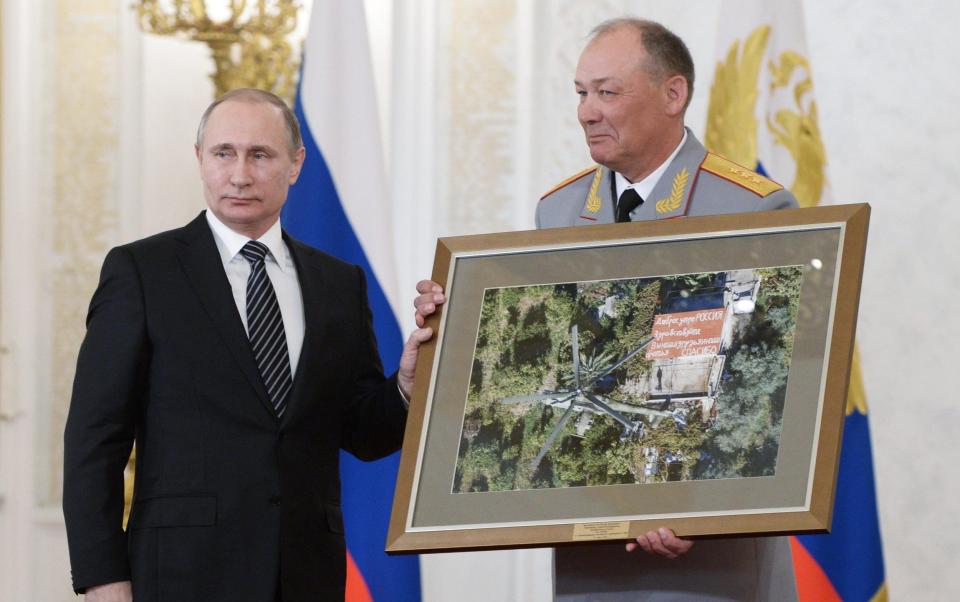 Vladimir Putin and Gen Dvornikov. They are holding a framed photograph showing a building in the Syrian countryside with a pro-Russian message on top