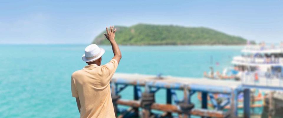 The traveler man standing on the boat waving his hand, greeting or goodbye to their friends on the pier.