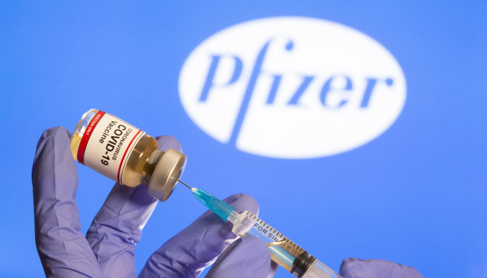 A woman holds a small bottle labeled with a "Coronavirus COVID-19 Vaccine" sticker and a medical syringe in front of displayed Pfizer logo in this illustration taken, October 30, 2020. REUTERS/Dado Ruvic