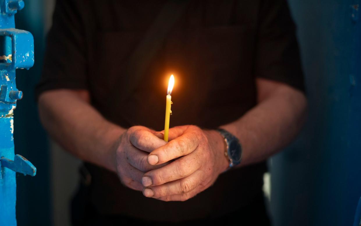 Father Andriy lights a candle in his church for fallen friends