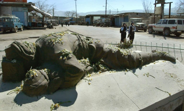 Iraqi Kurdish schoolgirls walk past a memorial of a dead Kurdish man protecting his child during the poison gas attack by Saddam Hussein's forces in 1988 in Halabja