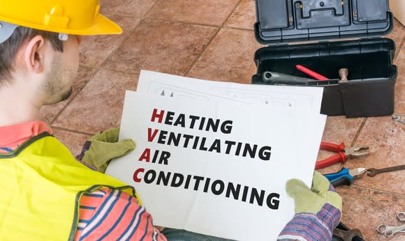 A man in a yellow hard hat and vest looking at a paper with heating, ventilating, and air conditioning written on it