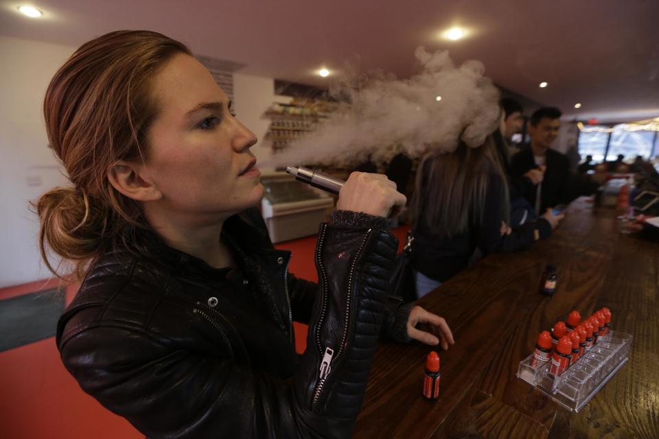 In this Feb. 20, 2014 photo, Talia Eisenberg, co-founder of the Henley Vaporium, uses her vaping device in New York. The vaporium is an intimate hipster hangout in the Soho neighborhood with overstuffed chairs, exposed brick, friendly counter help, but no booze. Instead, the proprietors are peddling e-cigarettes, along with bottles of liquid nicotine ready to be plucked from behind a wooden bar and turned into flavorful vapor for a lung hit with a kick that is intended to simulate traditional smoking. (AP Photo/Frank Franklin II)