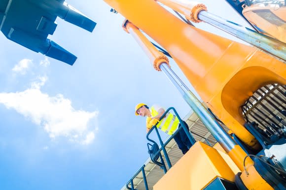 Worker in hard hat and safety vest standing next to big yellow excavating machine