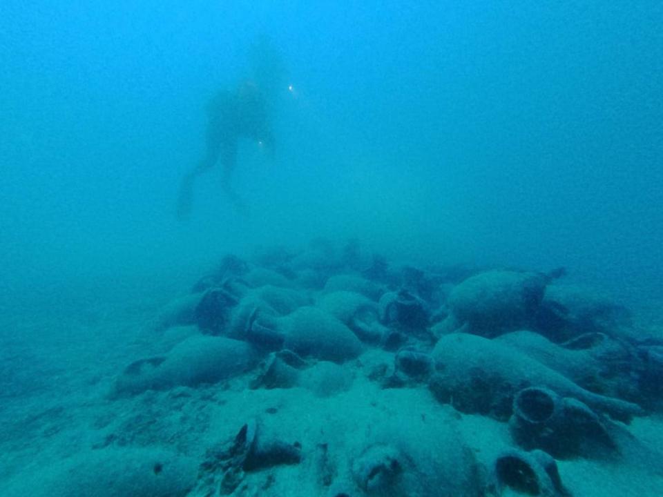 A scuba diver floats above the shipwreck and its cargo.