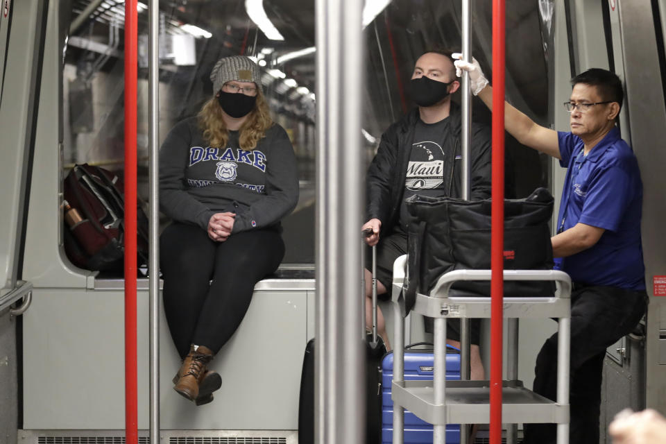 FILE - In this March 2, 2020 file photo, travelers Meredith Ponder, left, and Coleby Hanisch, both of Des Moines, Iowa, wear masks to remind them not to touch their faces as they ride a train at Seattle-Tacoma International Airport in SeaTac, Wash. The spread of the coronavirus, including cases in the U.S., has many small business owners canceling or changing plans, arranging for staffers to work from home, even asking employees who have traveled to places with widespread outbreaks to stay home for as long as a month. (AP Photo/Elaine Thompson, File)