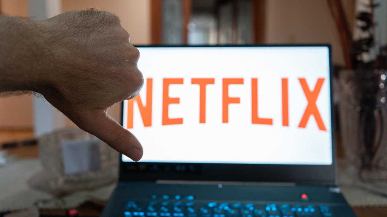  Hand making thumb down in front of a laptop showing the Netflix logo. 