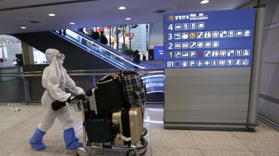 Eine Passagierin in Schutzkleidung schiebt am Flughafen Incheon einen Kofferwagen.