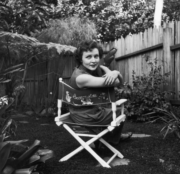 circa 1956: American actor Betty White sits in a canvas chair with her name written on the back, looking over her shoulder in a backyard garden. (Photo by Hulton Archive/Getty Images)