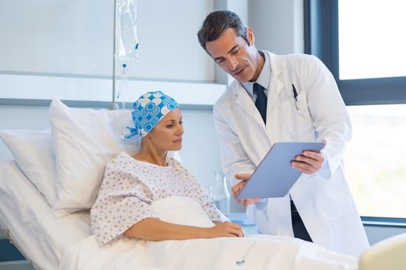 A male physician showing a bedridden female patient something on a clipboard.