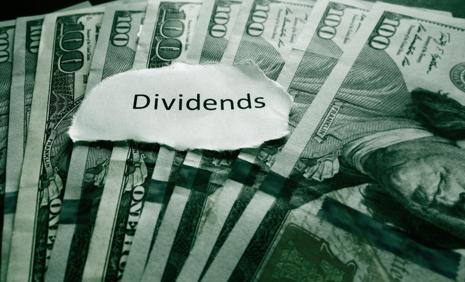 The word dividends written on a piece of paper resting on top of $100 bills