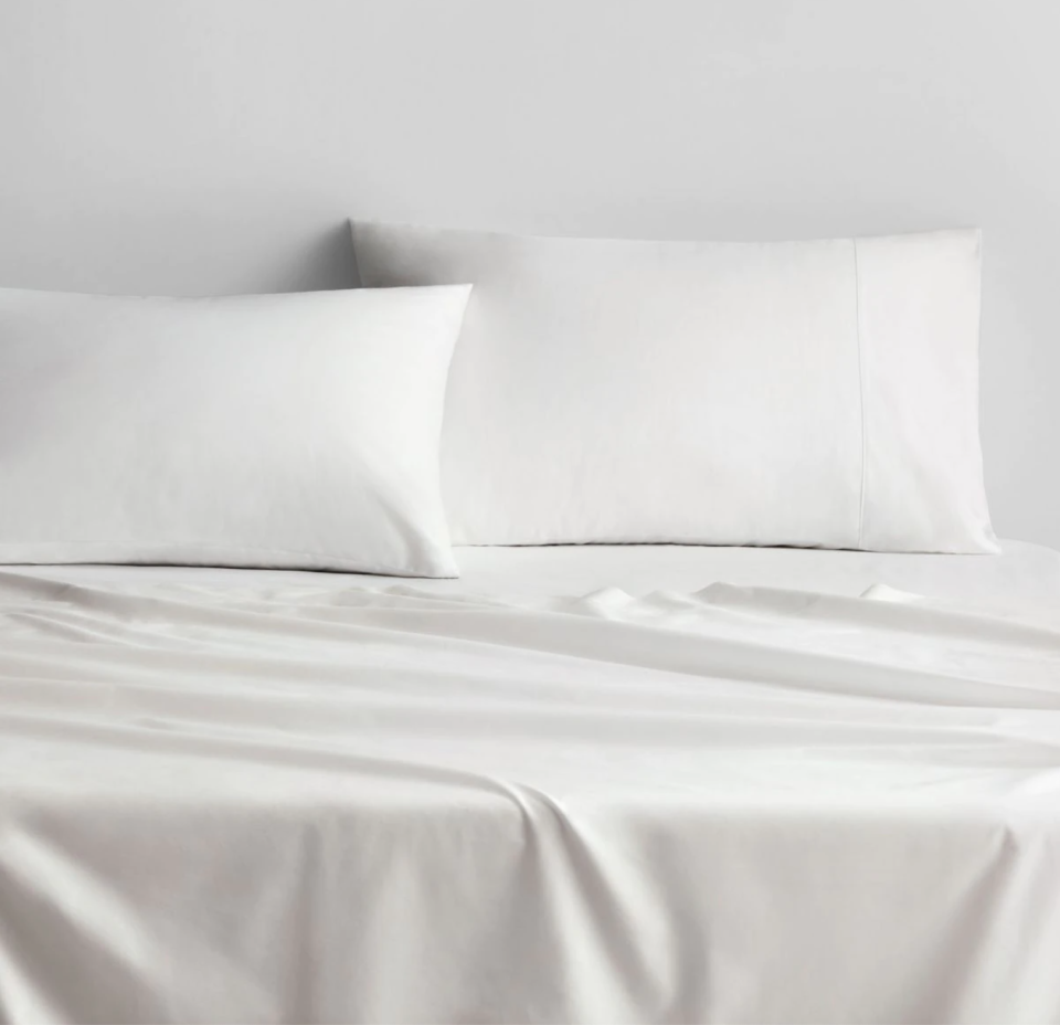 A bed made up in white linen against a white wall.