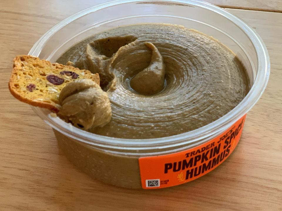 Clear container with orange label of Trader Joe's pumpkin-pie hummus with a cranberry crisp in it on a wooden table