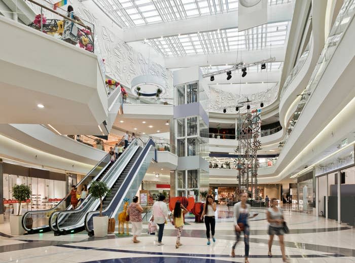 Interior of a multi-level shopping mall with shoppers, escalators, and storefronts