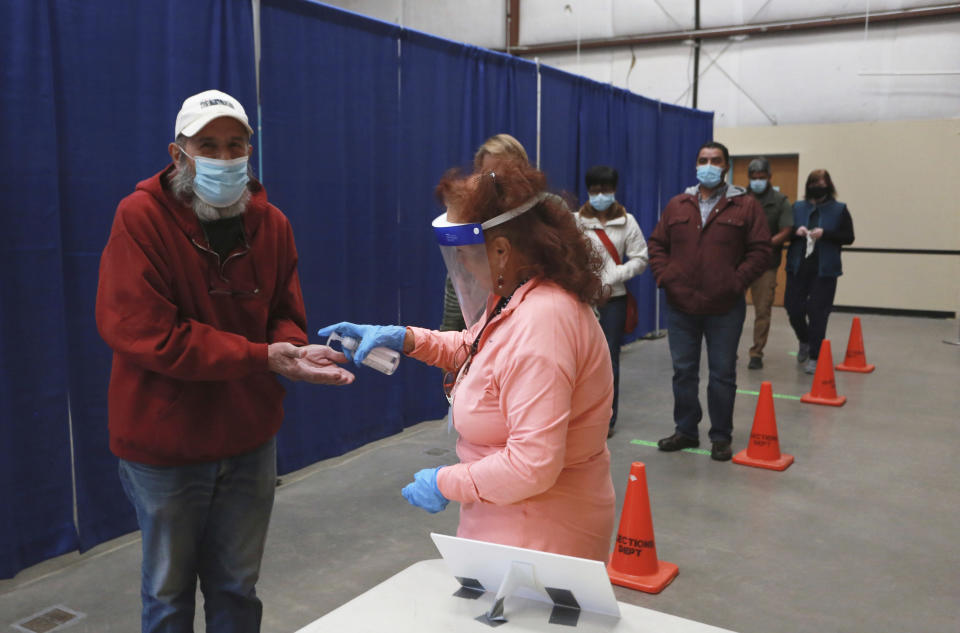 Dell Weston, left, holds out his hands to receive hand sanitizer from a poll worker at the fair grounds early voting center on Saturday, Oct. 17, 2020, in Santa Fe, N.M. Weston, a retired artist and metalworker, said he's a Republican plans to vote for Trump. He came for a sample ballot so that he could research down-ballot candidates and issues before he votes in person in the coming weeks. (AP Photo/Cedar Attanasio)