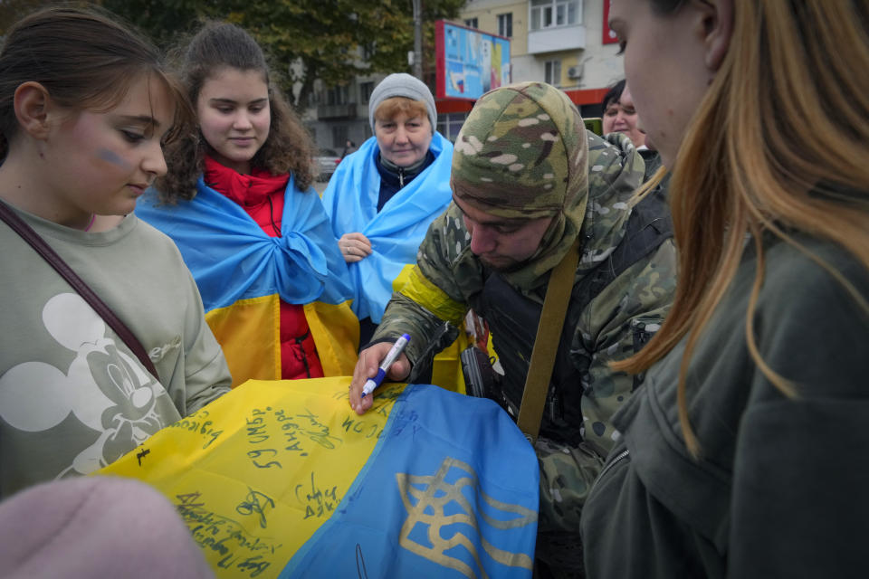 A Ukrainian soldier writes: "From the Ukrainian Armed Forces" on the national flag for a local resident in central Kherson, Ukraine, Sunday, Nov. 13, 2022. The Russian retreat from Kherson marked a triumphant milestone in Ukraine's pushback against Moscow's invasion almost nine months ago. (AP Photo/Efrem Lukatsky)