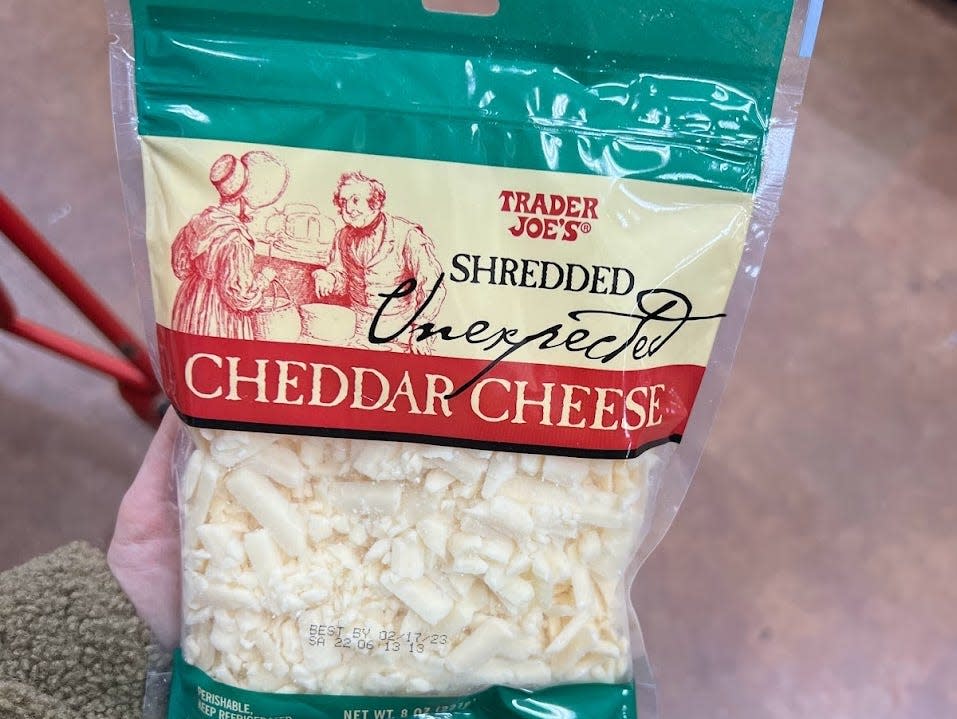The writer holds a bag of Trader Joe's shredded Unexpected cheddar cheese