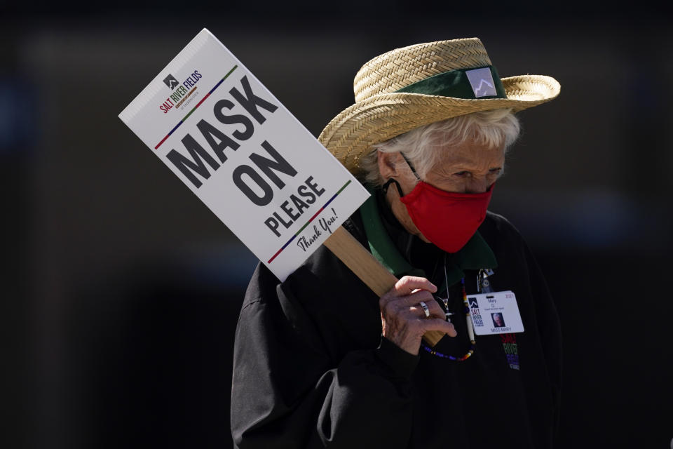 FILE - In this March 16, 2021, file photo, an usher holds a sign to remind fans to wear masks during a spring training baseball game between the Oakland Athletics and the Arizona Diamondbacks in Scottdale, Ariz. Arizona on Friday, Aug. 27, 2021, surpassed the milestone of 1 million confirmed coronavirus cases after the state reported 3,707 new infections amid continued wrangling over vaccinations and mask requirements. (AP Photo/Ashley Landis, File)
