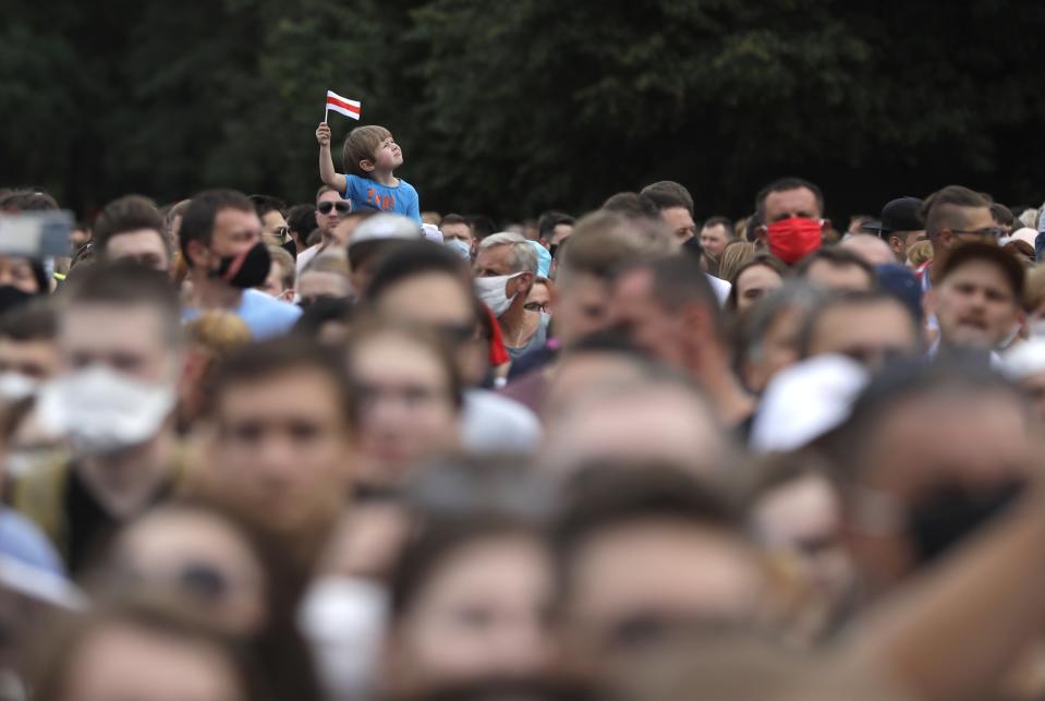 A child holds national flag as Belarusians listen to Svetlana Tikhanovskaya, candidate for the presidential elections, during a meeting with her supporters in Minsk, Belarus, Sunday, July 19, 2020. The presidential election in Belarus is scheduled for August 9, 2020. (AP Photo/Sergei Grits)