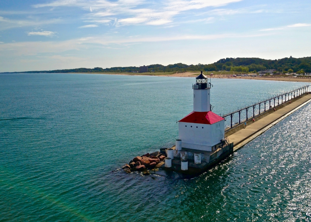 Lighthouse with a long boardwalk, sandy beaches with green trees in the background.