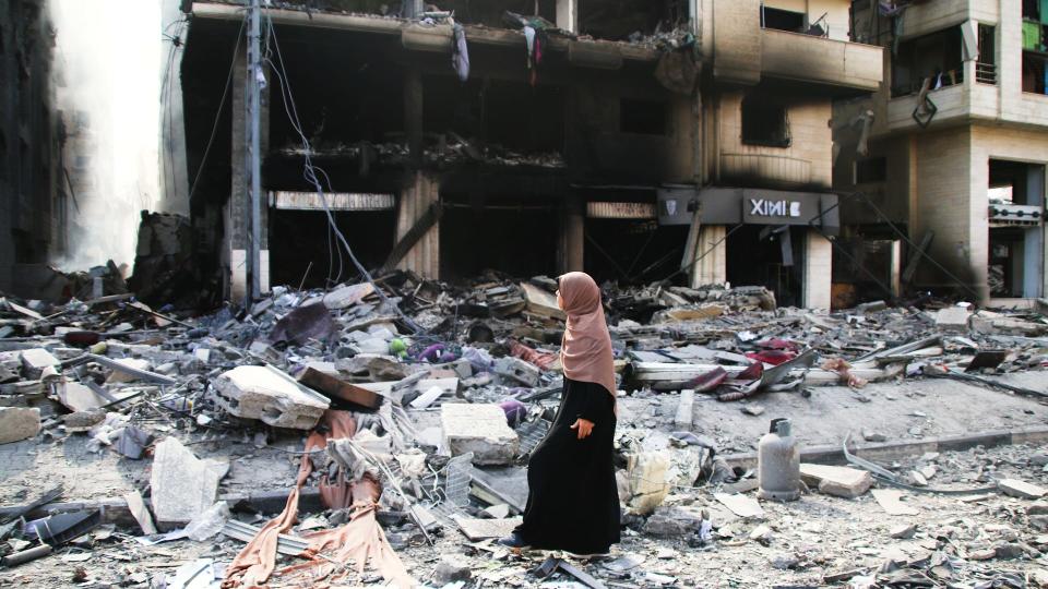 A Palestinian woman walks past damaged buildings from Israeli airstrikes on October 10, 2023 in Gaza City, Gaza.