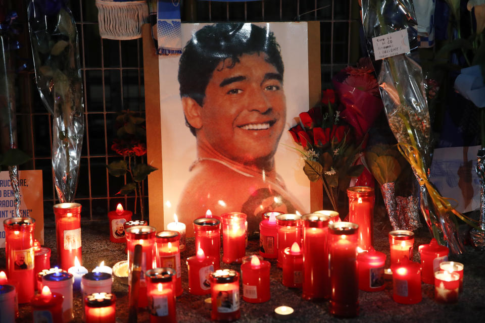 Candles and flowers are seen outside the San Paolo stadium commemorating soccer legend Diego Maradona, in Naples, Thursday, Nov. 26, 2020. Maradona died on Wednesday at the age of 60 of a heart attack in a house outside Buenos Aires where he recovered from a brain operation. (AP Photo/Alessandra Tarantino)