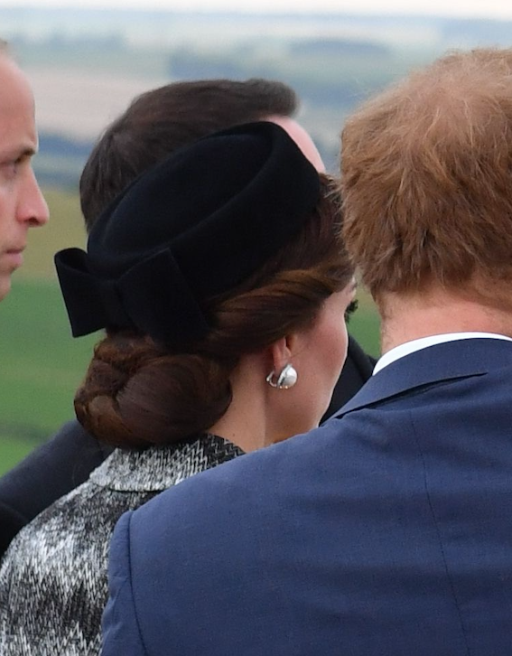 Three royals from behind, one wearing a black hat and earring, in a formal gathering