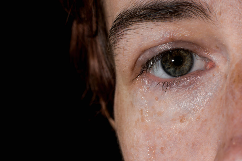 Closeup of one female eye and tear on her cheek.