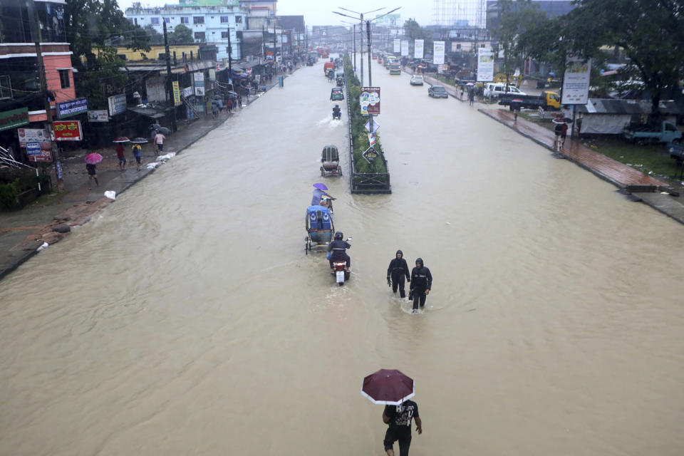 People wade through flooded waters in Sylhet, Bangladesh, Saturday, June 18, 2022. At least 18 people have died as floods cut a swatch across northeastern India and Bangladesh, leaving millions of homes underwater. Both countries have asked the military to help with the severe flooding, which could worsen because rains are expected to continue over the weekend. (AP Photo/Abdul Goni)