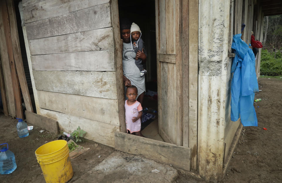 En esta imagen, tomada el 25 de mayo de 2019, una migrante haitiana lleva a su sobrino de cuatro meses en brazos mientras mira por la puerta de la casa de una familia embera en Bajo Chiquito, en la provincia de Darién, Panamá. Los residentes cobran tres dólares diarios a los migrantes por el privilegio de alojarse en sus viviendas. (AP Foto/Arnulfo Franco)