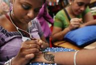 Tatuadoras indias trazan diseños de henna en las manos de sus clientes. (AP Photo/Wong Maye-E)