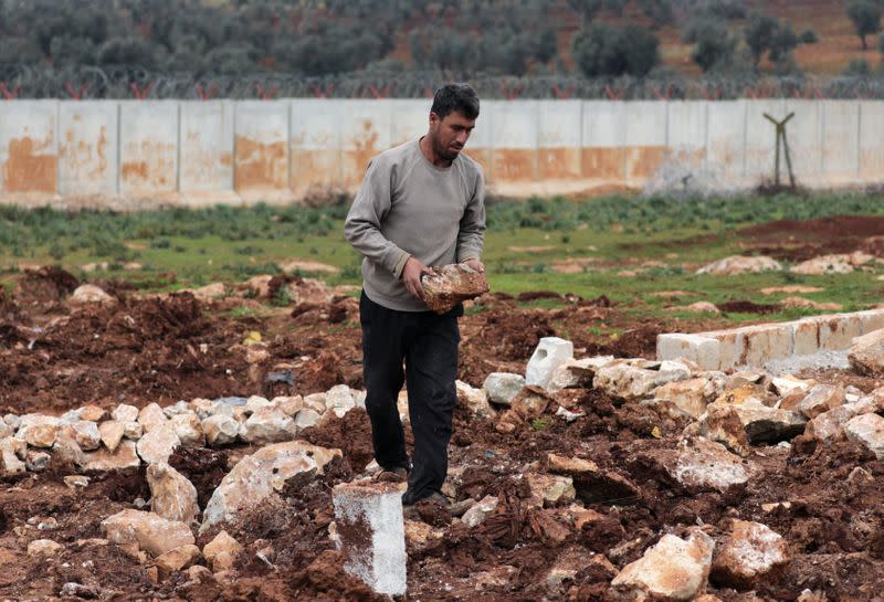 An Internally displaced Syrian man holds a rock as he puts up a tent near the wall in Atmah IDP camp, located near the border with Turkey