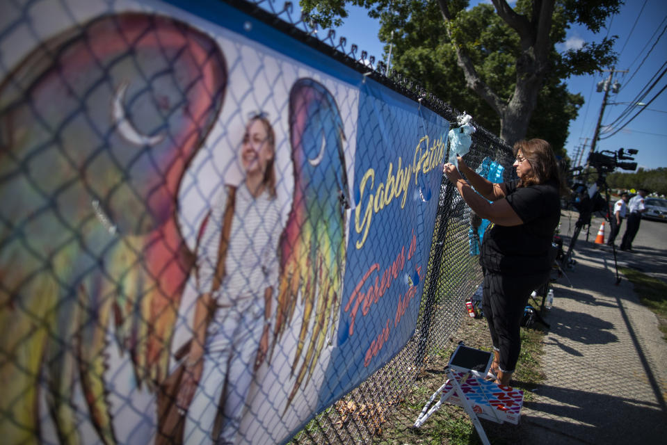 CORRECTS TO FUNERAL HOME VIEWING INSTEAD OF FUNERAL A woman places a decoration near a poster after attending the funeral home viewing of Gabby Petito at Moloney's Funeral Home in Holbrook, N.Y. Sunday, Sept. 26, 2021. (AP Photo/Eduardo Munoz Alvarez)