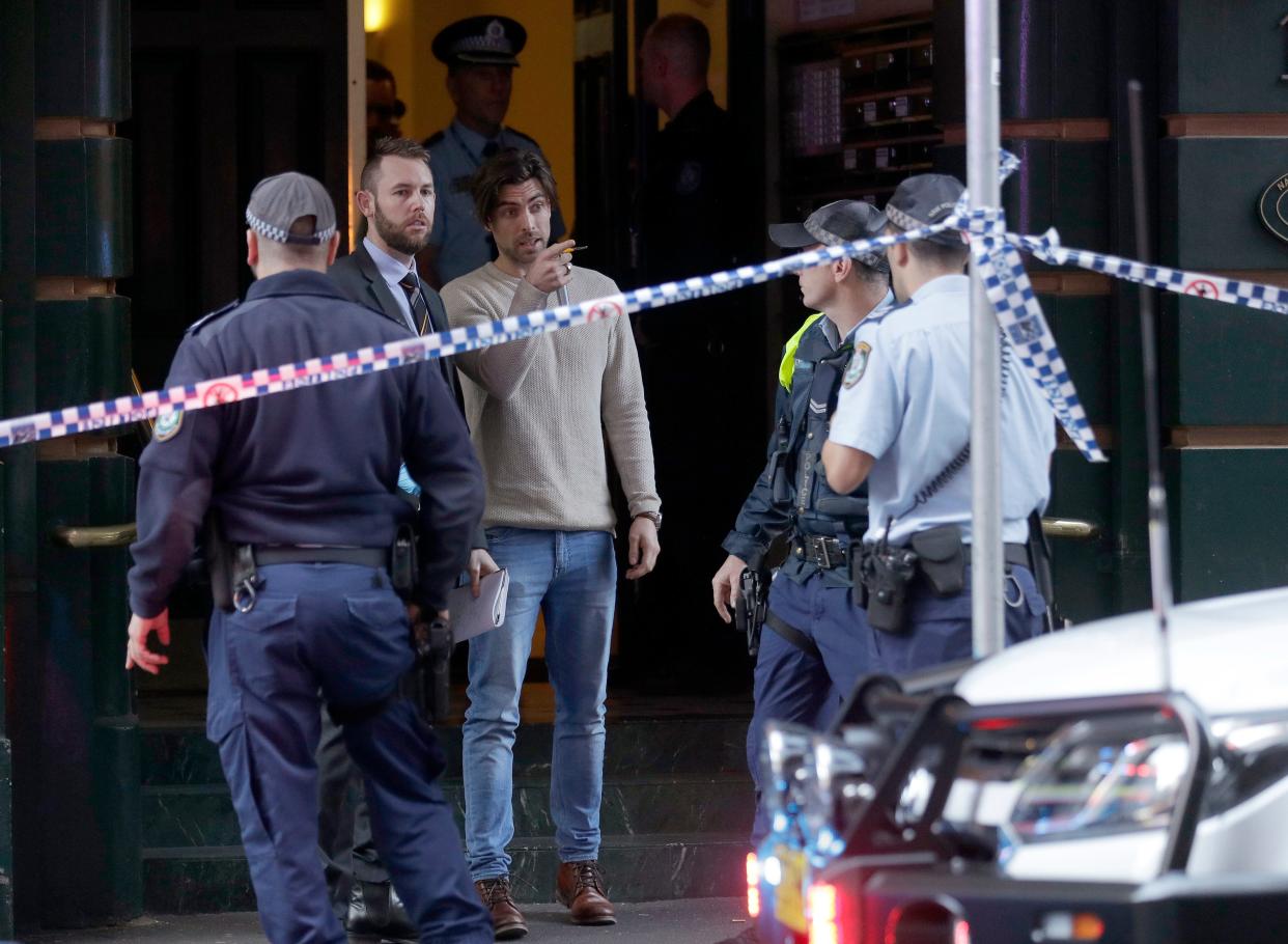 A man, center, points as he assists police at a building where a person has been found deceased after a man attempted to stab multiple people in Sydney, Australia, Tuesday, Aug. 13, 2019.