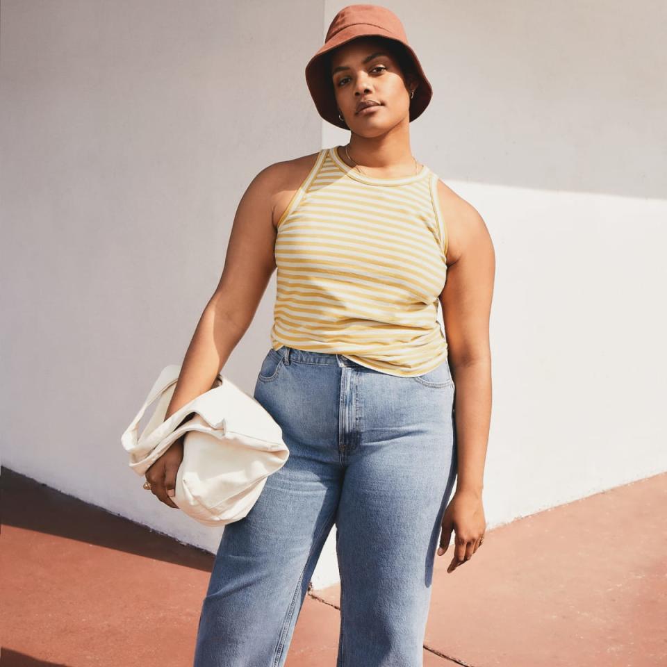 Model wears The Organic Cotton Cutaway Tank in yellow stripe with blue jeans. Image via Everlane.