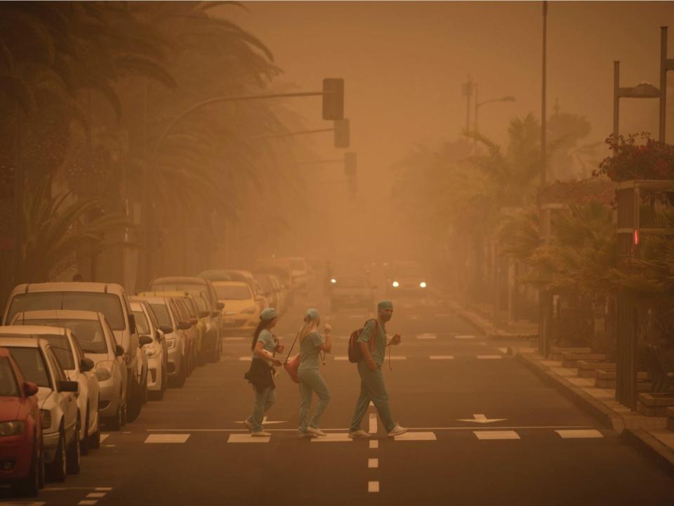 People in carnival dress walk across a street crossing in a cloud of red dust in Santa Cruz de Tenerife, Spain, Sunday, Feb. 23, 2020.