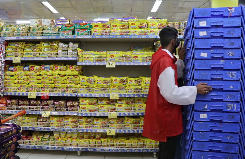 A worker pushes shopping baskets next to packets of Nestle's Maggi noodles and Reliance's Snac tac noodles inside a Reliance supermarket in Mumbai